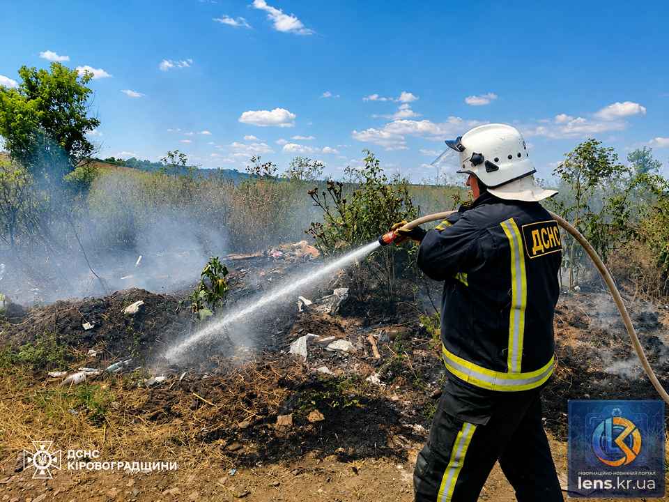 Рятувальники за допомогою спецобладнання гасять палаючу суху траву на полі.